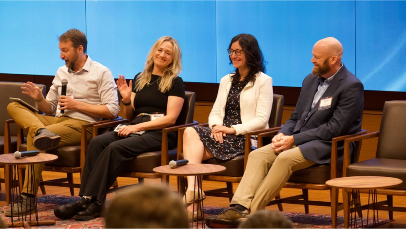 Four people sitting next to each other on a conference stage.